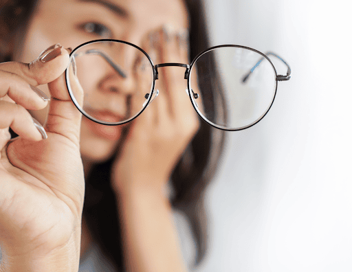 Woman_holding_eyeglasses_with_blurred_face_in_background