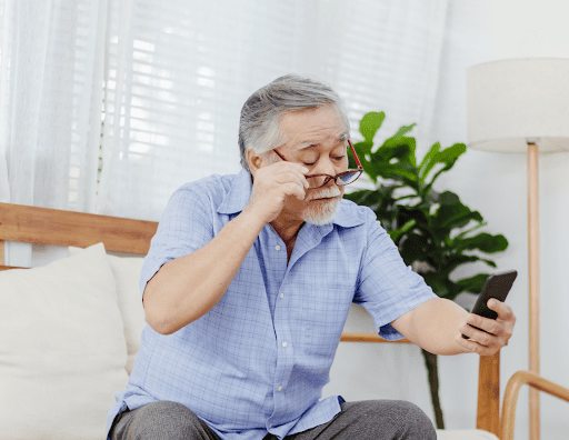 Elderly_Asian_man_adjusting_glasses_while_looking_at_smartphone